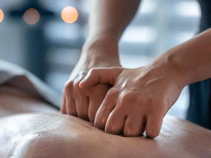 Mãos aplicando pressão firme sobre as costas de uma pessoa deitada, em sessão de terapia manual